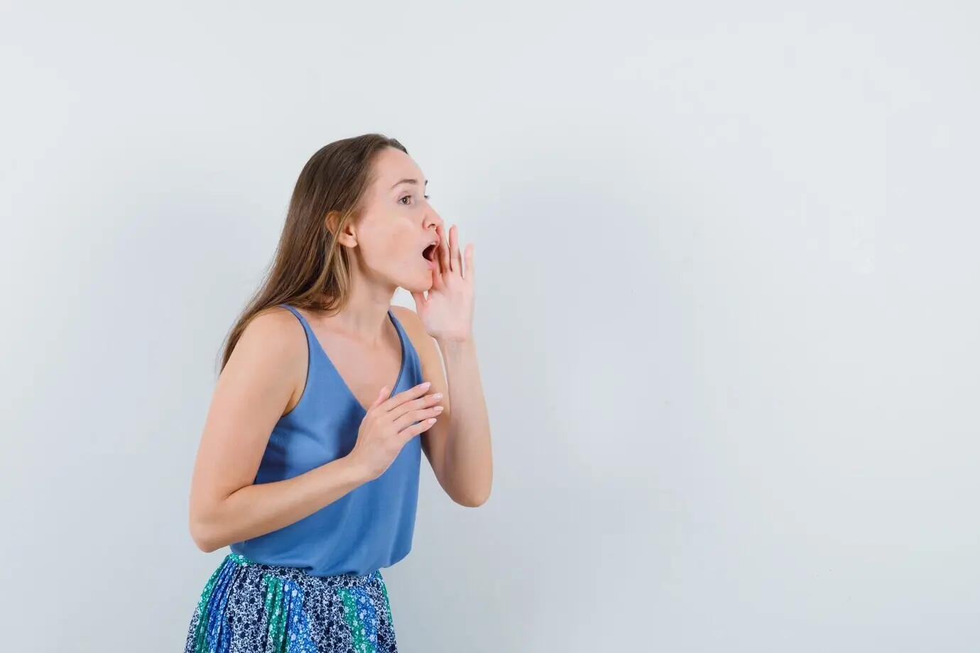 Молодая девушка в синей блузке и юбке громким голосом зовёт кого‑то и смотрит осторожно, вид спереди.