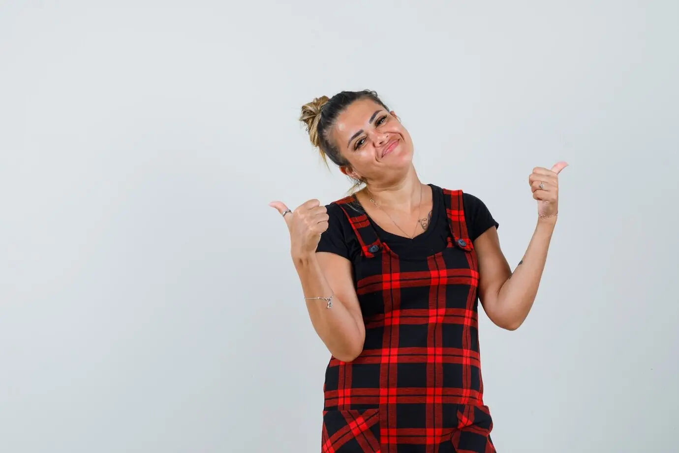 Женщина в платье-сарафане показывает два больших пальца вверх и выглядит весёлой, вид спереди.