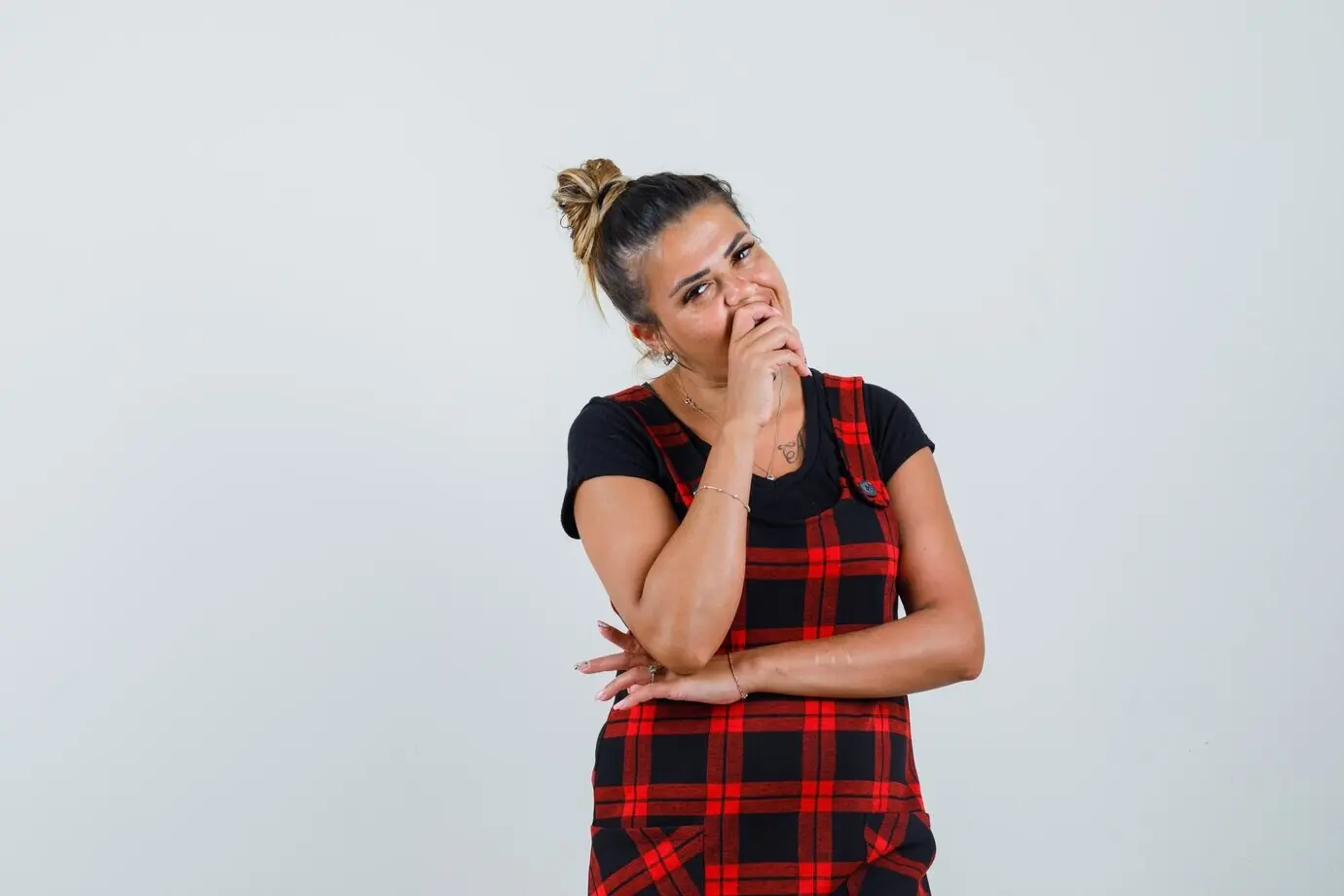 Женщина в платье-сарафане держит руку на подбородке и смотрит задумчиво, вид спереди.