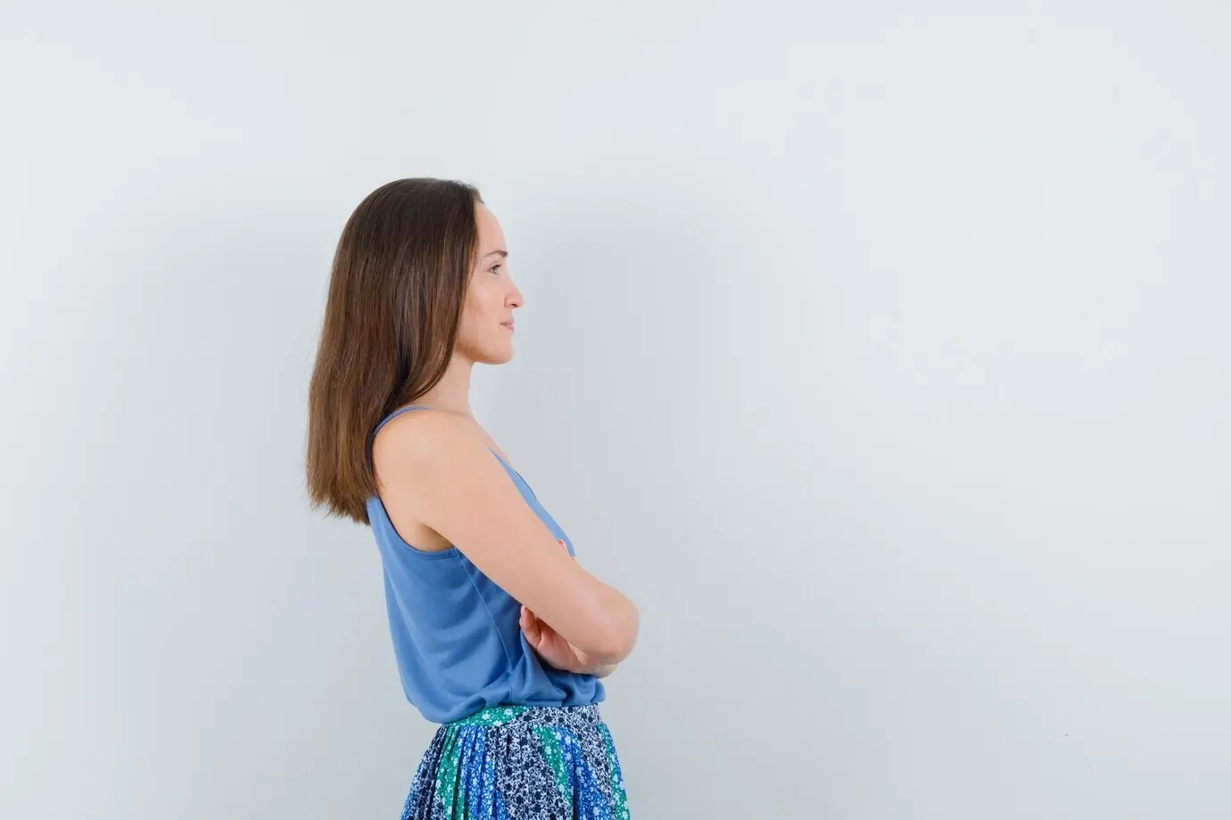 Молодая женщина стоит со скрещенными руками в блузке и юбке.