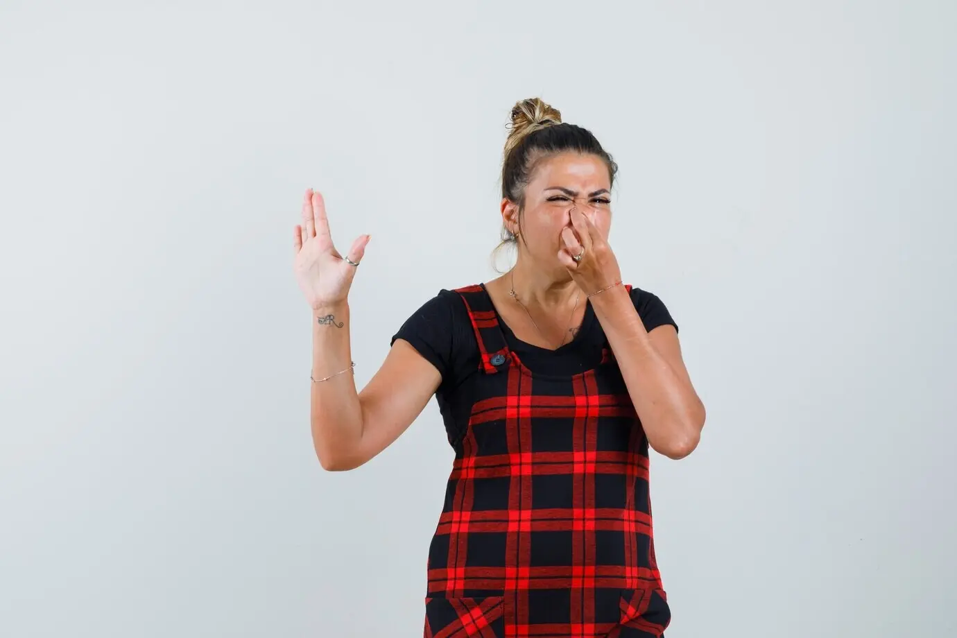 Женщина в платье-сарафане зажимает нос из-за неприятного запаха, с выражением отвращения; вид спереди.